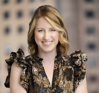 The image shows a smiling woman with long, wavy blonde hair wearing a patterned blouse. The woman appears to be the person named Laura O'Donnell