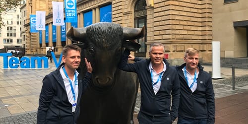 A group of men standing in front of a TeamViewing logo next to a bull sculpture. 