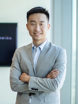 Chenxing Yu, a young, smiling Asian man in a gray suit, standing with his arms crossed in a professional setting