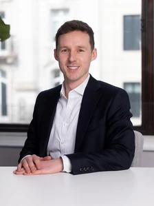Toby Hunston, a professional-looking man in a suit, sitting at a desk and smiling at the camera in a business setting