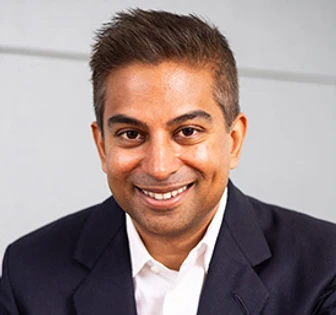 A smiling man in a navy blue suit, looking directly at the camera with a warm expression