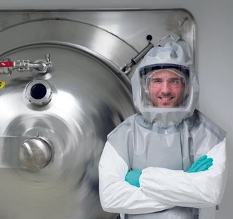 A man in a white protective suit stands in front of a large industrial tank, his face covered with a transparent mask. The image is titled "cambrex 3"