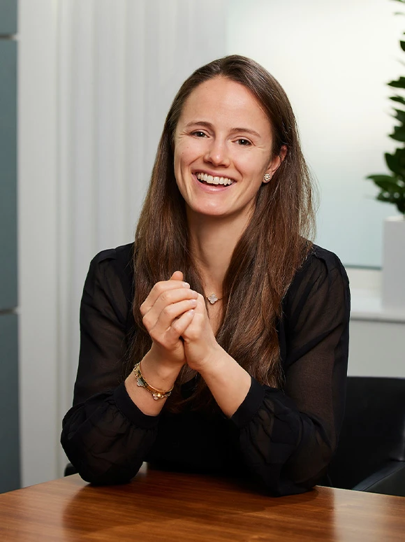 Nina Suter, a smiling woman with long brown hair, sits at a desk in a bright, professional environment