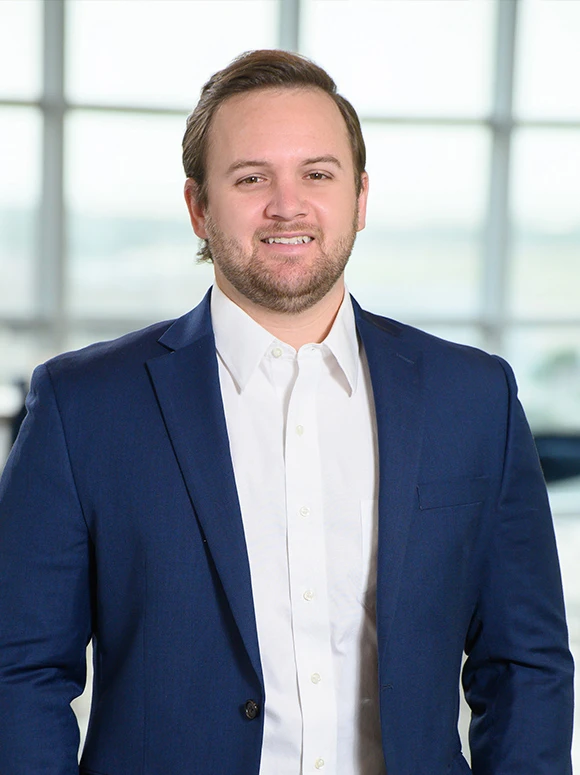 Portrait of a businessman with a beard wearing a navy blue suit and white shirt, standing in front of a glass window