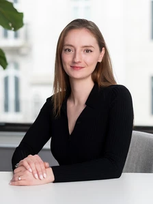 Fran, a woman with long brown hair, poses for a professional portrait wearing a black pleated blouse and smiling confidently at the camera