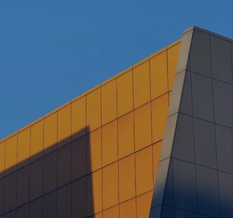 This image depicts a geometric, angular building facade with a striking contrast between the dark gray panels and the vibrant yellow accents against a clear blue sky