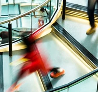 A blurred image of people walking quickly on an escalator in a modern, glass-enclosed indoor space