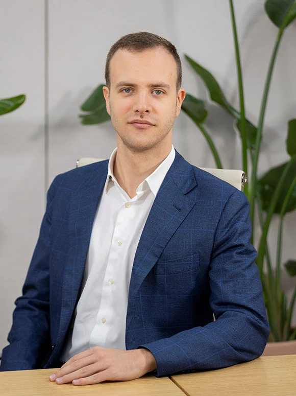 The image shows Aurelio Pappalardo, a man in a blue suit, sitting at a desk with green plants in the background. He has a serious expression and appears to be in a professional setting