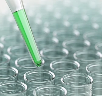 The image shows a glass laboratory test tube filled with a green liquid, surrounded by a field of other clear test tubes, conveying a scientific or medical research context