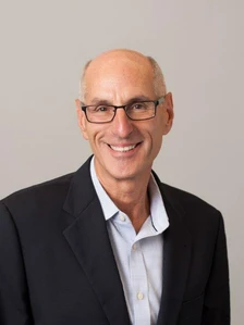 Bruce Citizen, a smiling, bespectacled man in a suit and collared shirt, appears in a headshot-style portrait