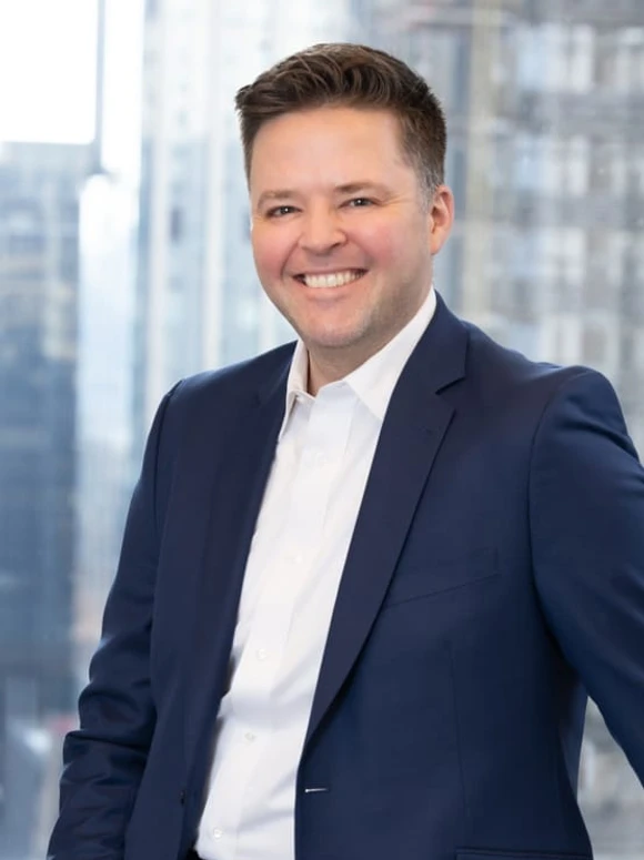 A smiling man in a business suit, identified as Justin Herridge, posing against a background of city skyscrapers