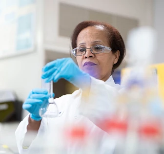 An experienced female scientist wearing a white lab coat and blue gloves, carefully handling lab equipment in a research facility
