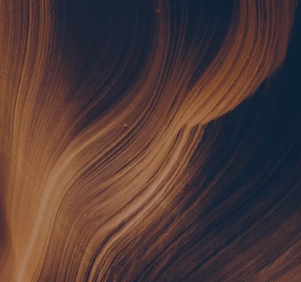 The image shows close-up waves of dark and light auburn-colored hair flowing in a stream-like pattern against a dark background
