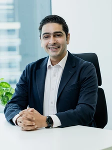 A smiling young professional man wearing a suit and sitting at a desk in an office setting