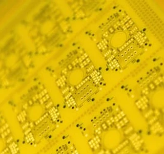 The image shows a close-up of a yellow printed circuit board or microchip, with intricate patterns and small components visible