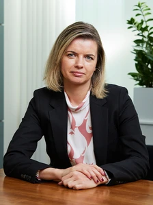 Michaela Rajnohova, a professional woman with blonde hair and blue eyes, sitting at a desk and wearing a black suit