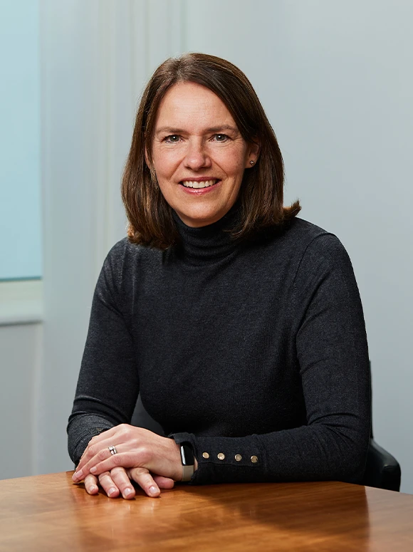 The image shows Julie Gray, a professional-looking woman in her 40s or 50s, smiling and sitting at a desk against a light blue background