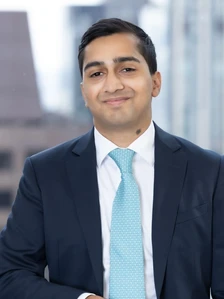 Mathew Roy, a business professional in a navy blue suit and teal tie, smiling confidently in an urban setting