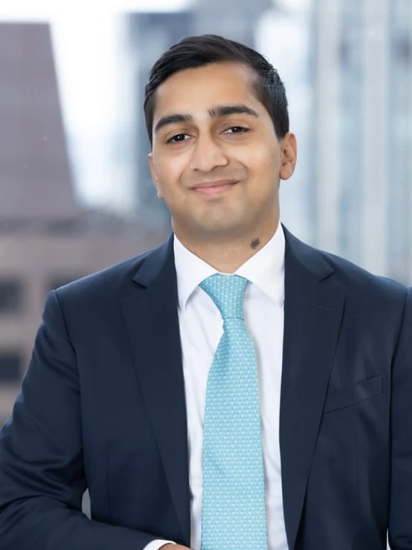 Mathew Roy, a business professional in a navy blue suit and teal tie, smiling confidently in an urban setting
