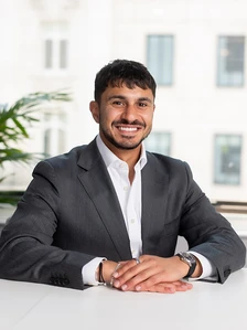 Nadir Hemnani, a smiling businessman in a gray suit, sitting at a desk in a modern office setting
