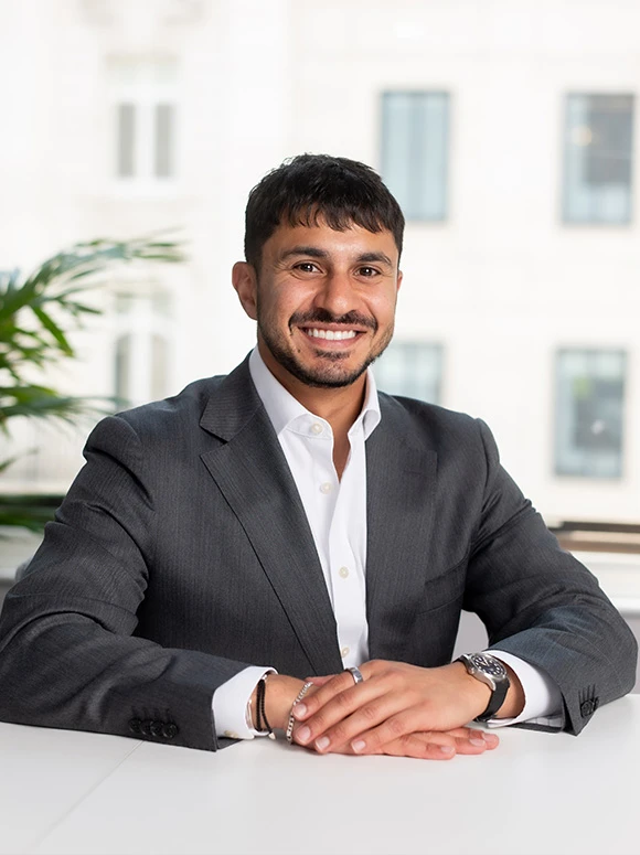 Nadir Hemnani, a smiling businessman in a gray suit, sitting at a desk in a modern office setting