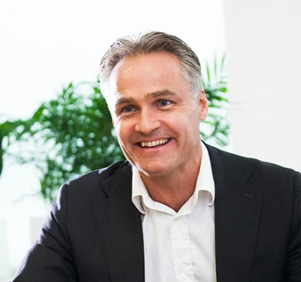 Kurt, a middle-aged man with gray hair, is smiling warmly in a professional headshot against a backdrop of greenery