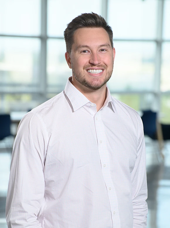 The image shows Jude Allen, a smiling businessman wearing a white shirt and standing in a modern office environment