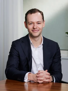 Portrait of Tom Goldsworthy, a man in a business suit, sitting at a desk with a serious and confident expression